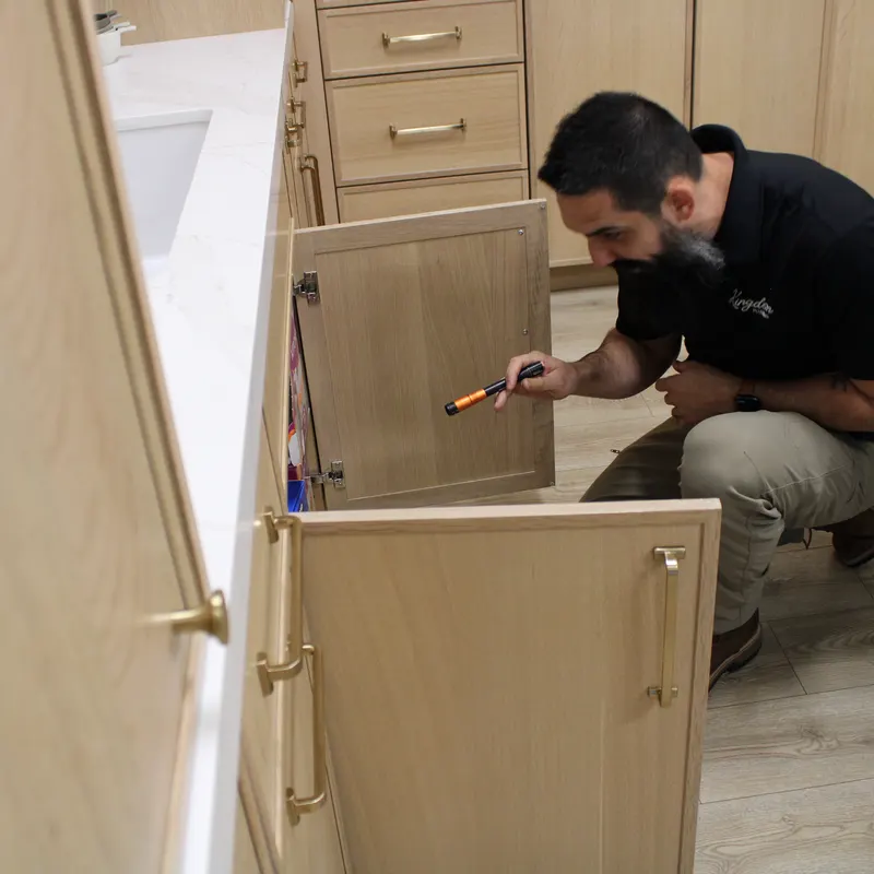 Kingdom Plumbing tech doing water leak detection under a kitchen sink with a flashlight
